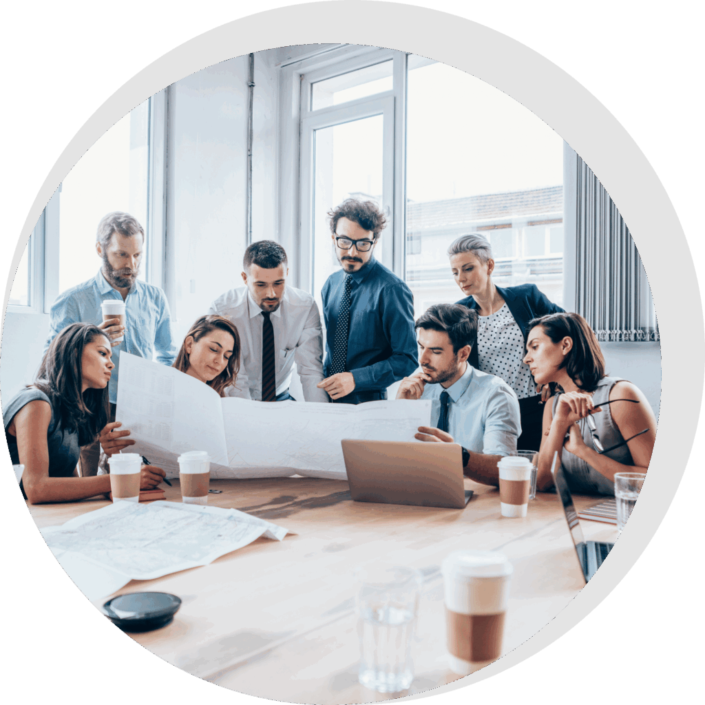 SGO-Immo-Simon-Gogel- Eine Gruppe von acht Personen in Geschäftskleidung versammelt sich um einen Tisch in einem modernen Reutlinger Büro-Besprechungszimmer und bespricht Dokumente und Laptop-Details - vielleicht planen sie die Instandhaltung für eine lokale Hausverwaltung. Kaffeetassen und Papiere sind vor ihnen ausgebreitet.